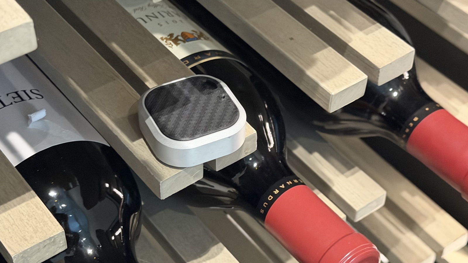 A Puk wireless sensor resting on a wooden wine rack between bottles