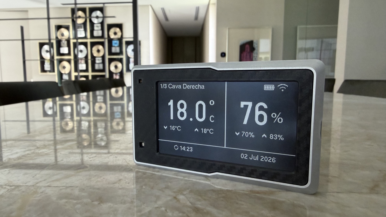 The Tali e-paper display on a marble table, showing 18.0°C and 76% humidity for a wine cellar